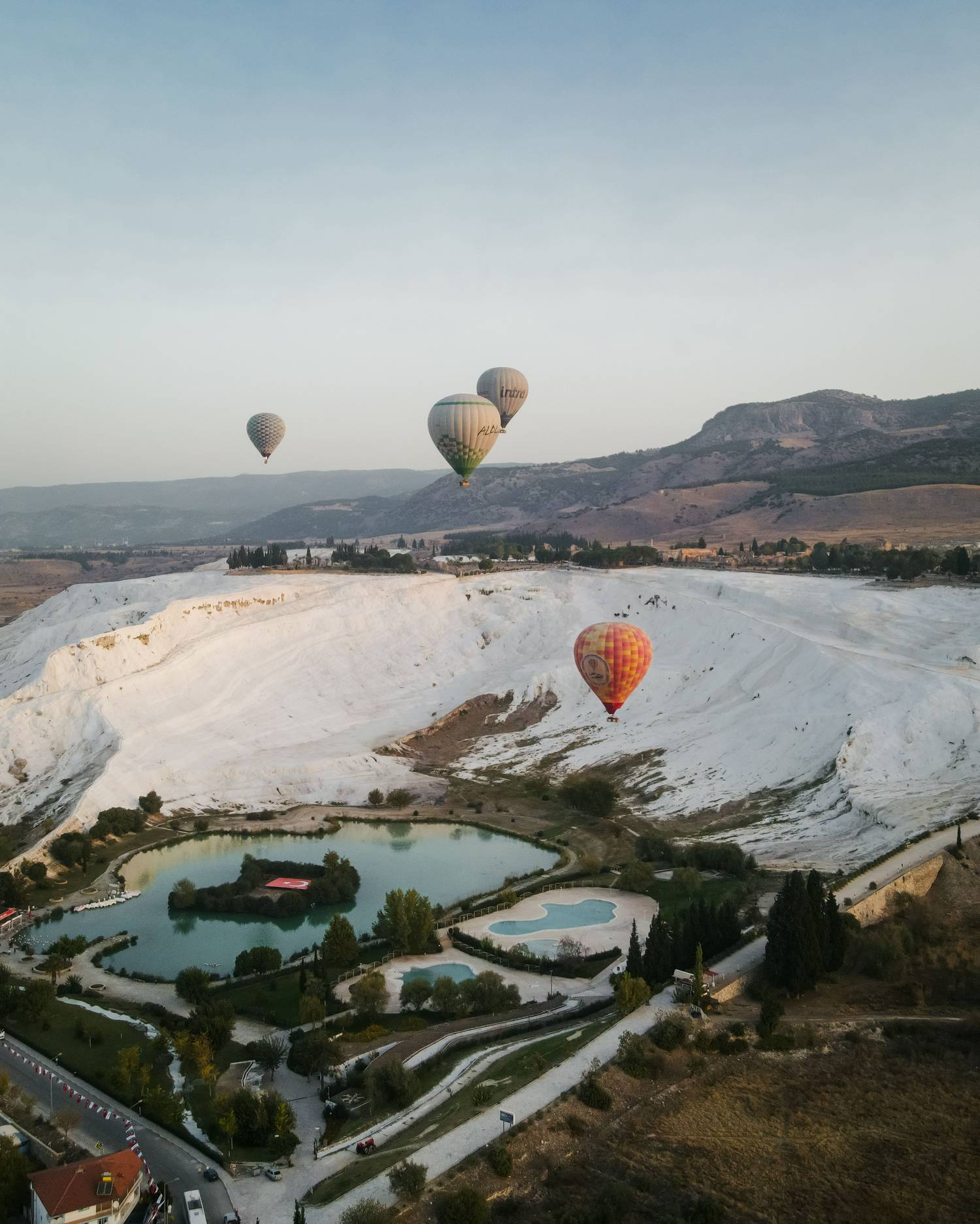 Hot air balloons rising in the early light above the white terraces of Pamukkale